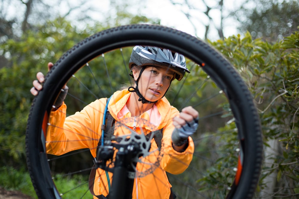 Female biker repairing mountain bike in countryside