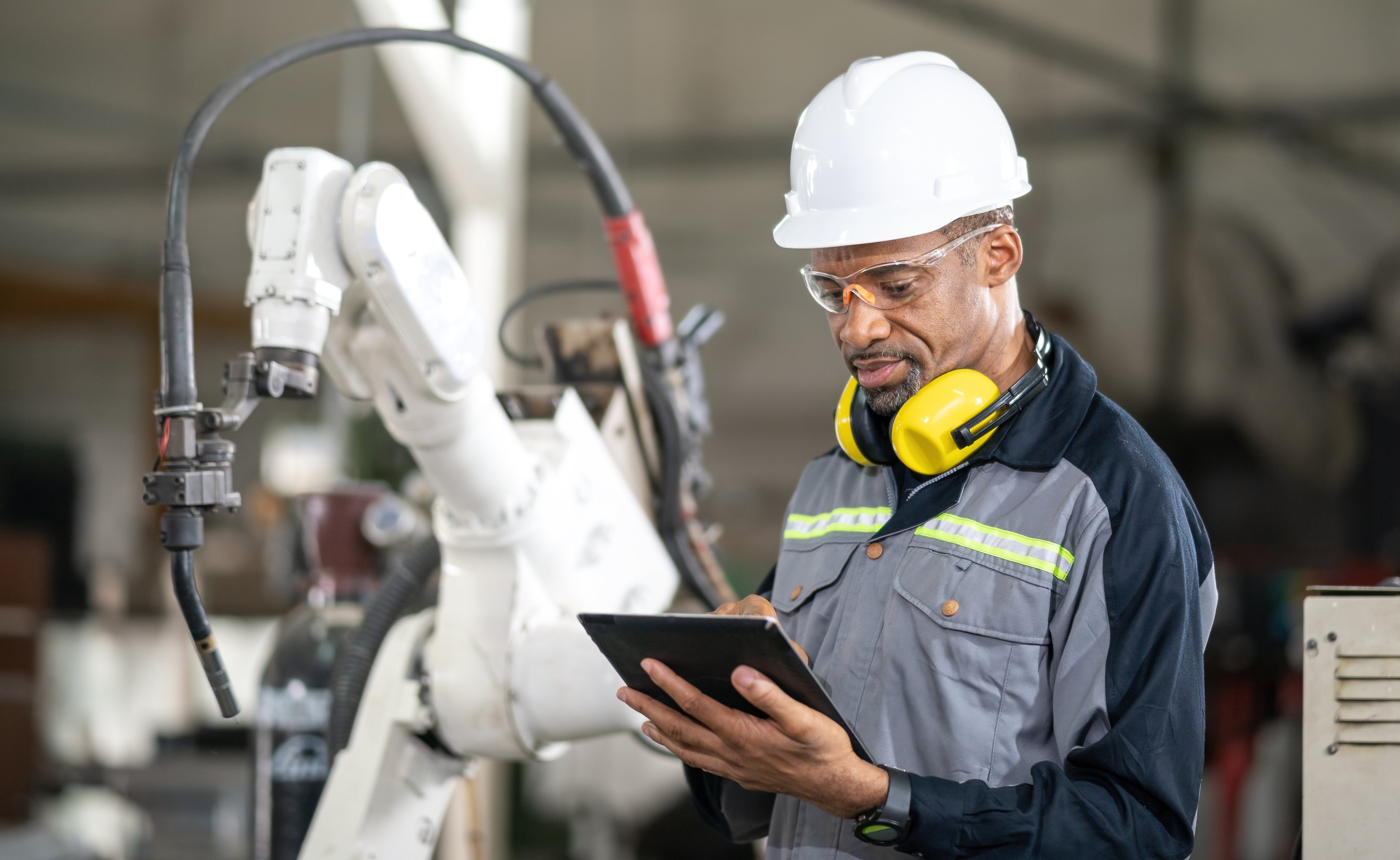 Arbeiter mit weißem Helm und Tablet vor einer Maschine