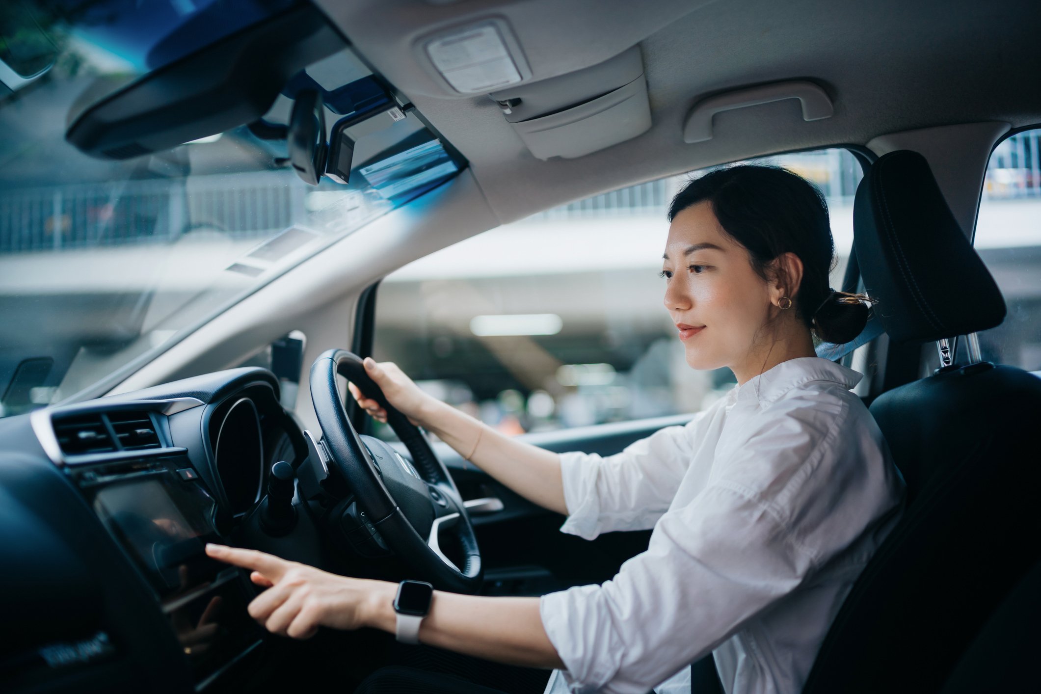 Junge Frau sitzt in einem Auto hinter dem Lenkrad und tippt auf das Display.