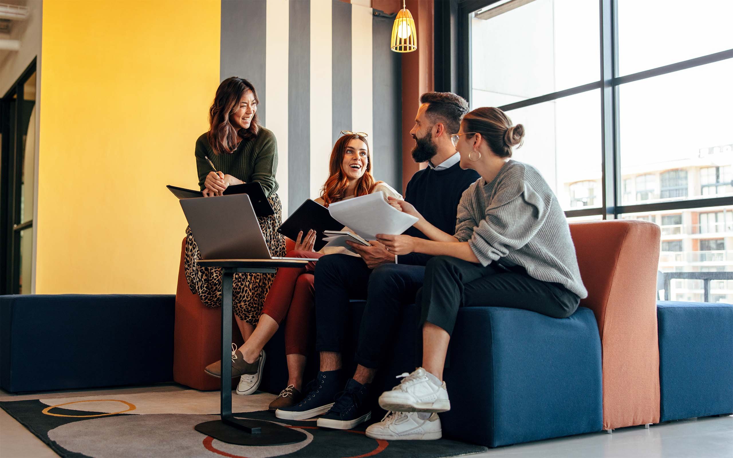 Drei Frauen und ein Mann sitzen auf Sofa und schauen auf Laptop und Unterlagen